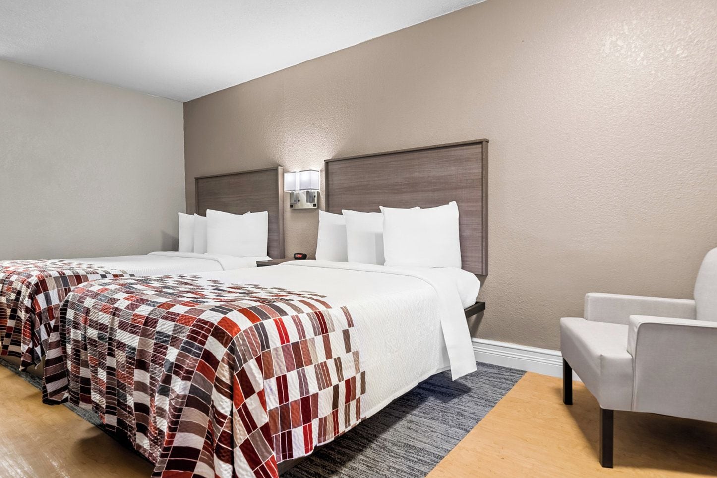 A hotel room with two beds, a gray carpet, and a white armchair.