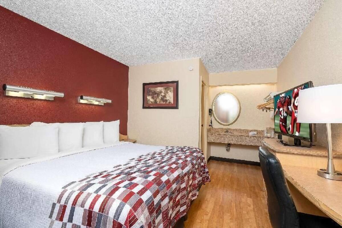 A hotel room with a bed, a mirror, a television, and a red accent wall.