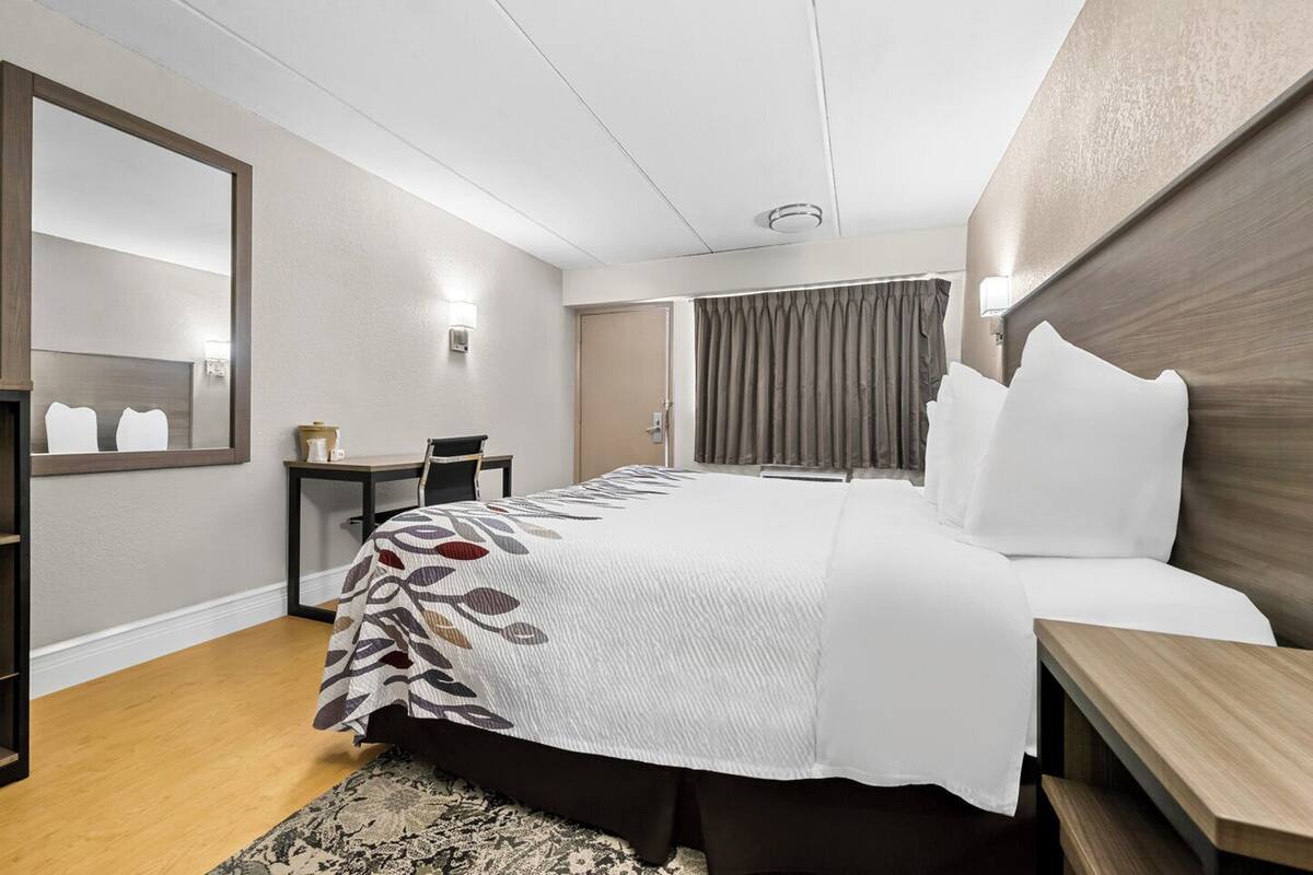A hotel room with a large bed, a desk, a chair, a mirror, and a window with curtains.