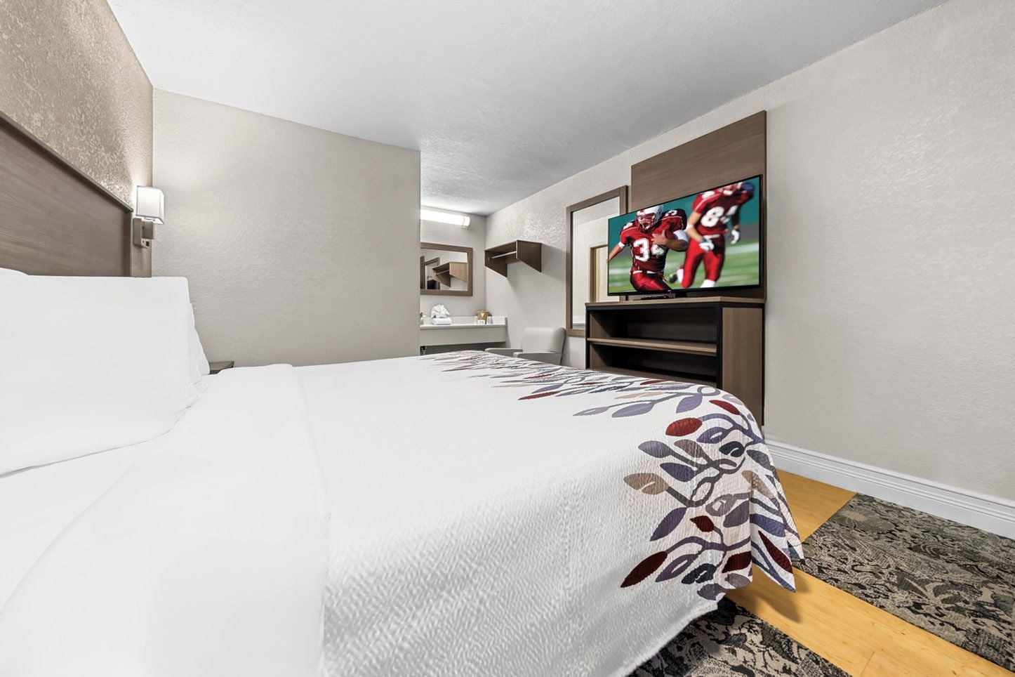 Une chambre d’hôtel avec un lit, une télévision, un bureau et une salle de bain que l’on aperçoit à l’arrière-plan.