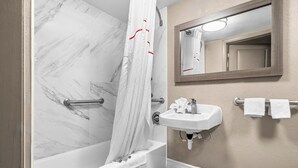 A bathroom with a marble shower wall, a white bathtub, a sink with a mirror above it, and a towel rack with two towels. - Red Roof Inn Tampa Fairgrounds – Casino (Tampa)