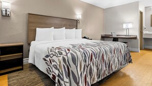 A hotel room with a large bed, a bedside table, a desk with a lamp, and a bathroom visible through an open door. - Red Roof Inn Tampa Fairgrounds – Casino (Tampa)