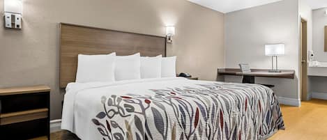 A hotel room with a large bed, a bedside table, a desk with a lamp, and a bathroom visible through an open door.