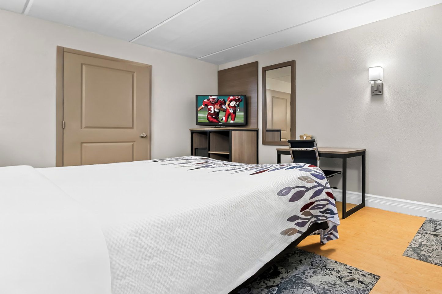 Ein Hotelzimmer mit Bett, Schreibtisch, Fernseher und Spiegel.