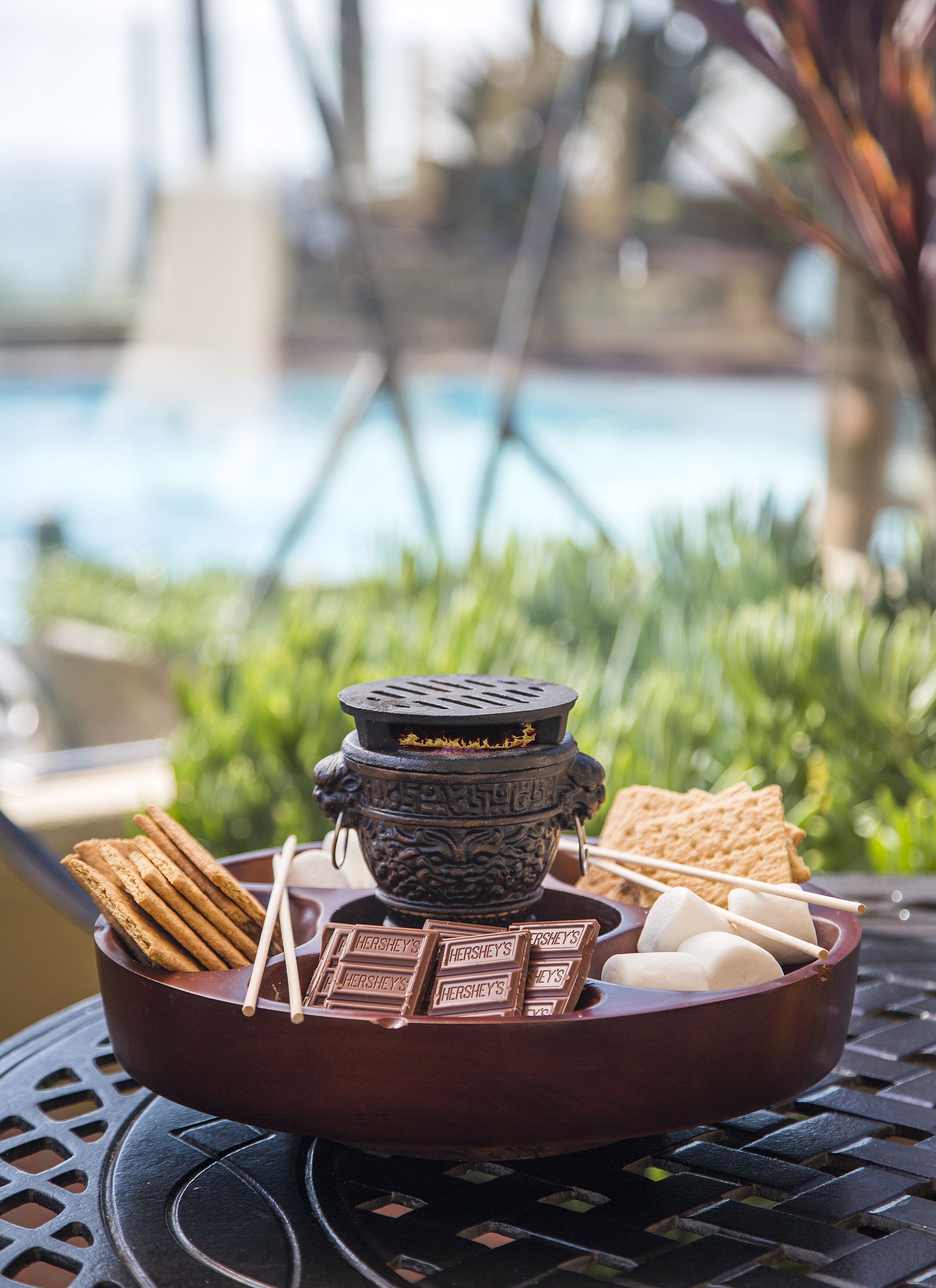 A chocolate fondue setup with marshmallows and crackers on a table by a pool.