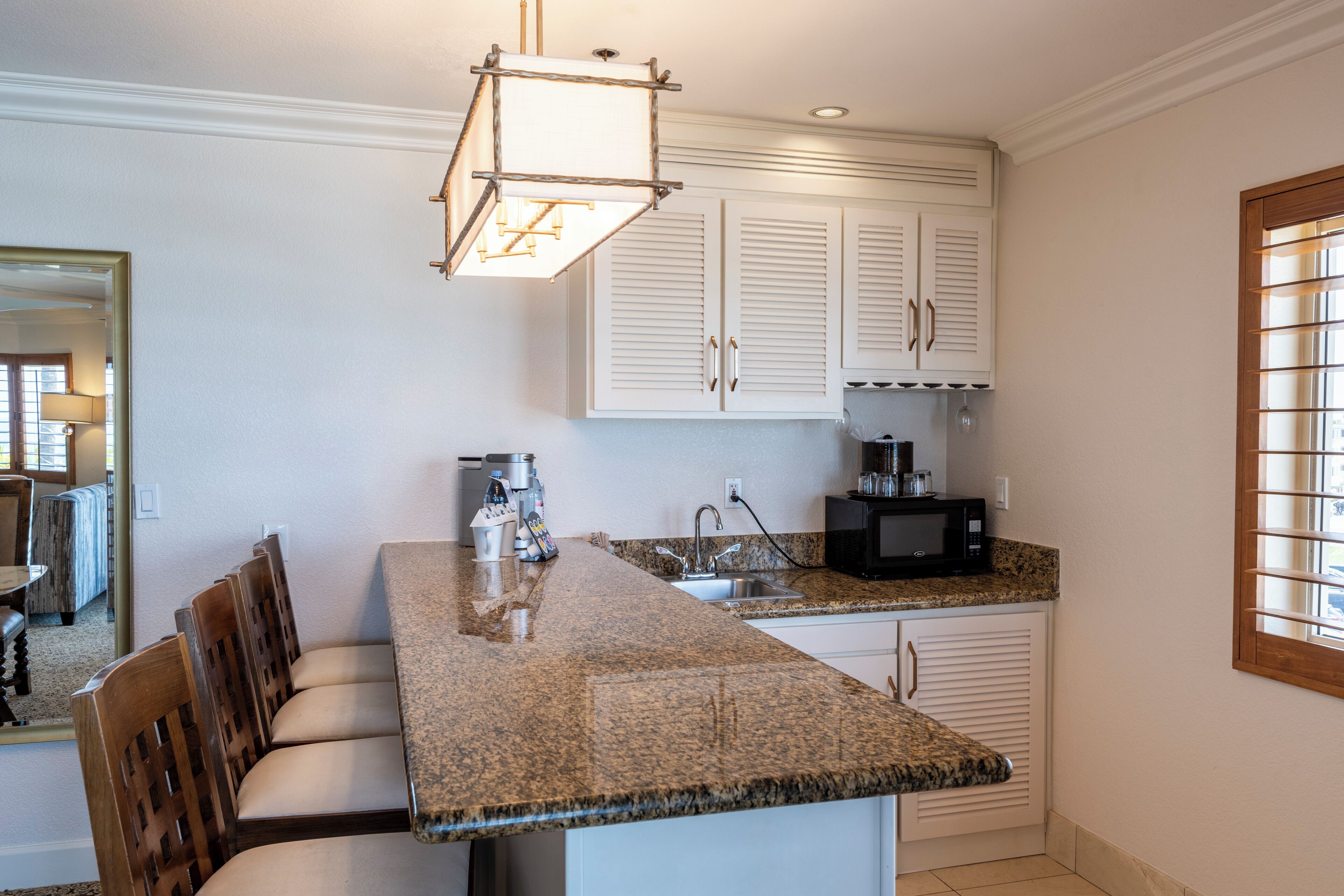A kitchen with a granite countertop, white cabinets, a built-in microwave, and a hanging light fixture.