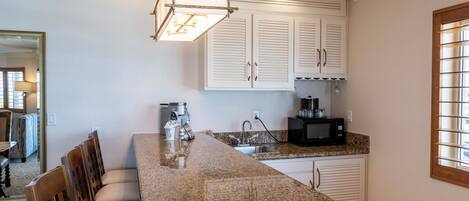 A kitchen with a granite countertop, white cabinets, a built-in microwave, and a hanging light fixture.