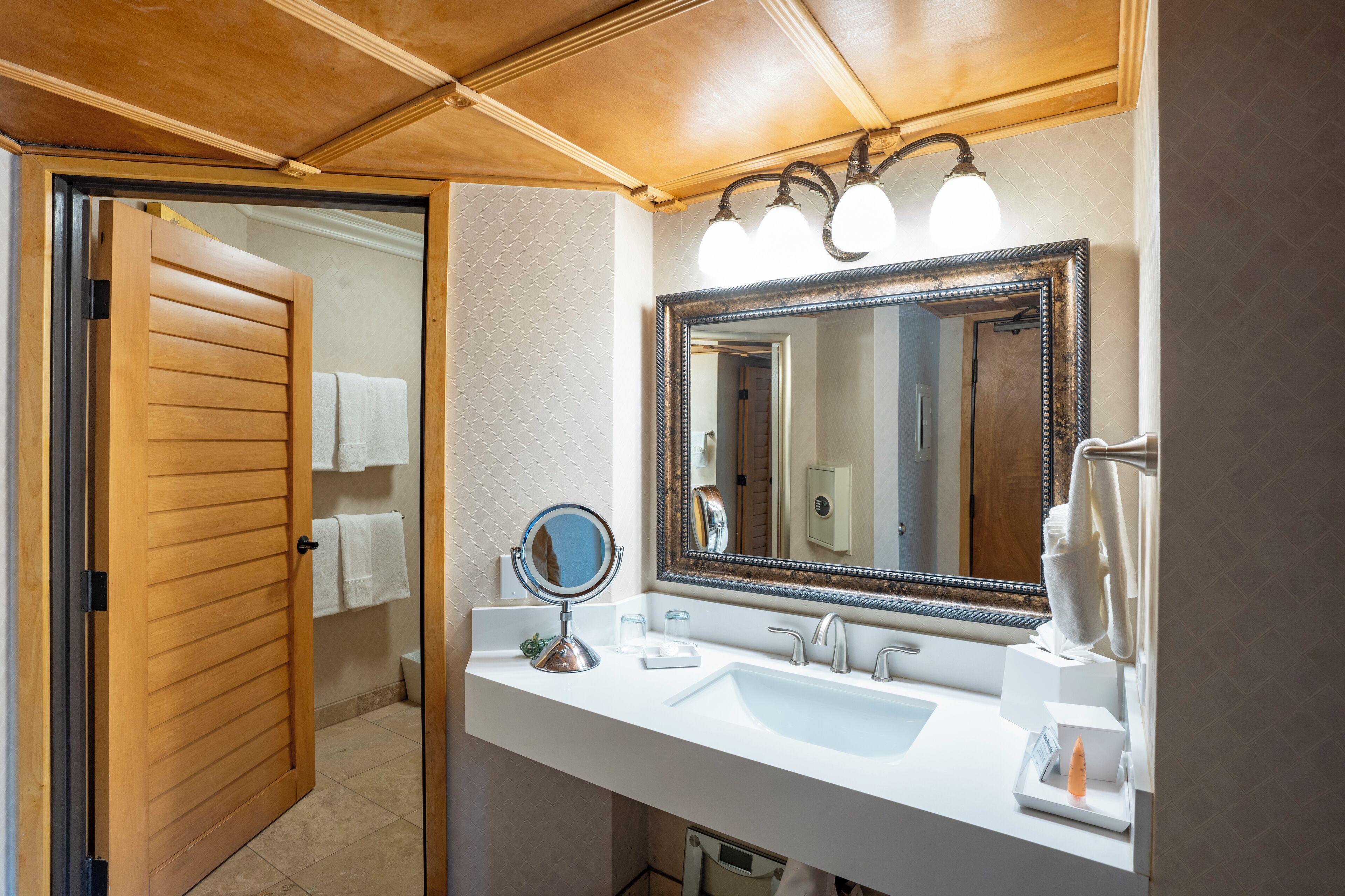 Ein Badezimmer mit Holztür, großem Spiegel, Waschbecken und Handtuchhalter.