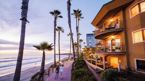 A beachfront hotel with a balcony overlooking the ocean, a walkway lined with palm trees, and a view of the beach. - Pacific Terrace Hotel (San Diego)