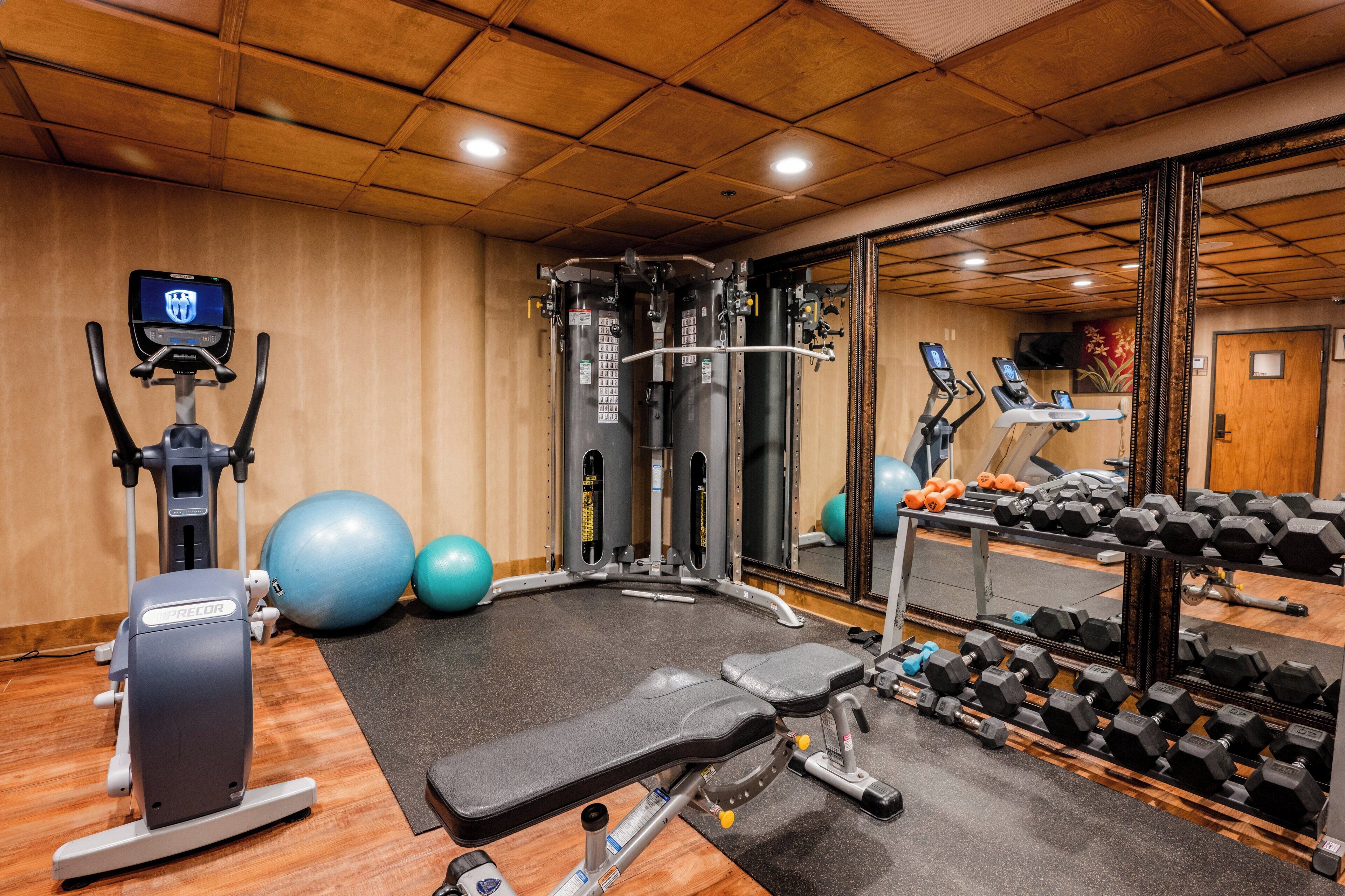 Ein Fitnessraum mit Trainingsgeräten, einem Spiegel und einem an der Wand befestigten Bildschirm.