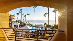 A pool area with umbrellas, palm trees, and a view of the ocean.
