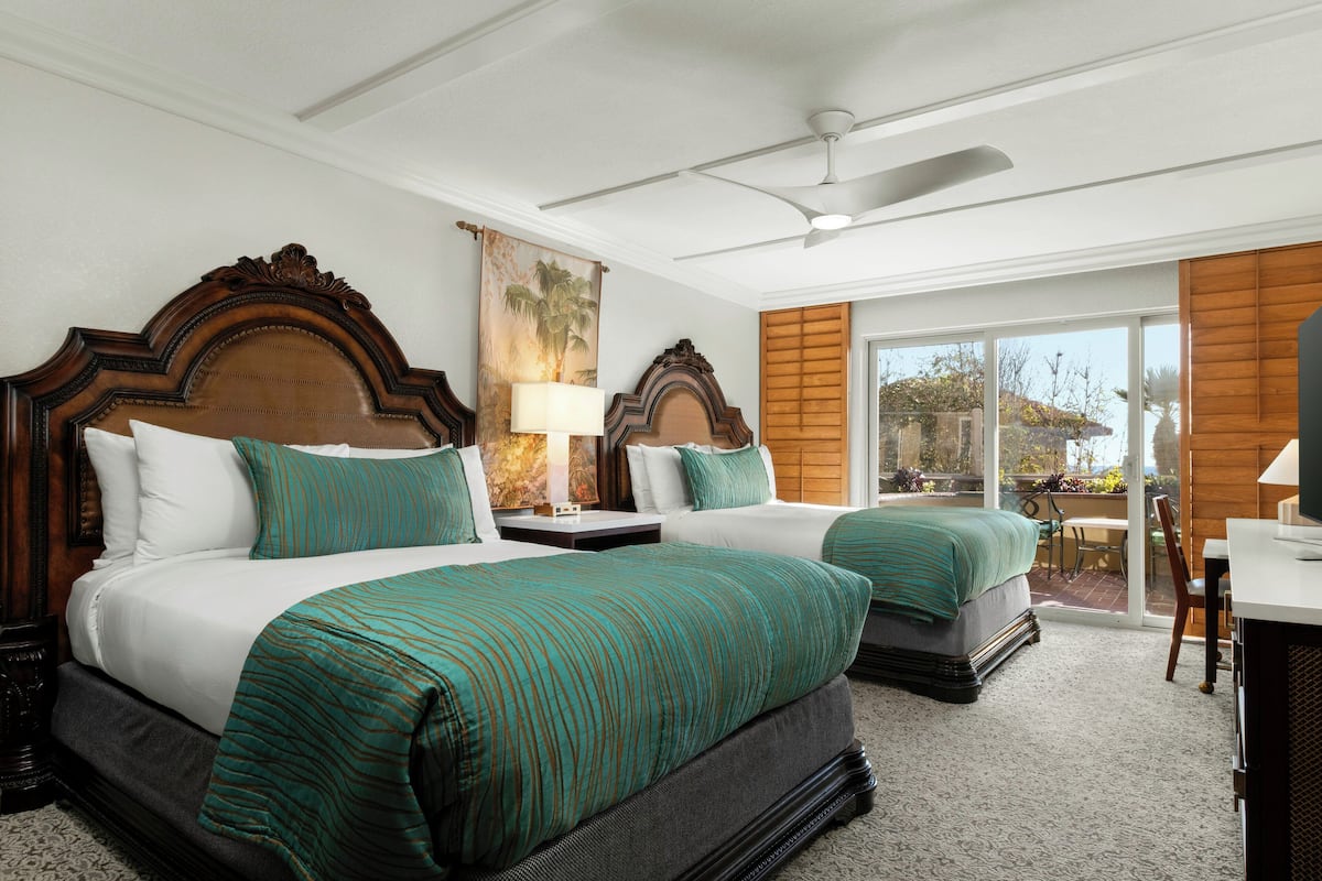 A hotel room with two beds, a ceiling fan, a large window with a view, and a wooden headboard.
