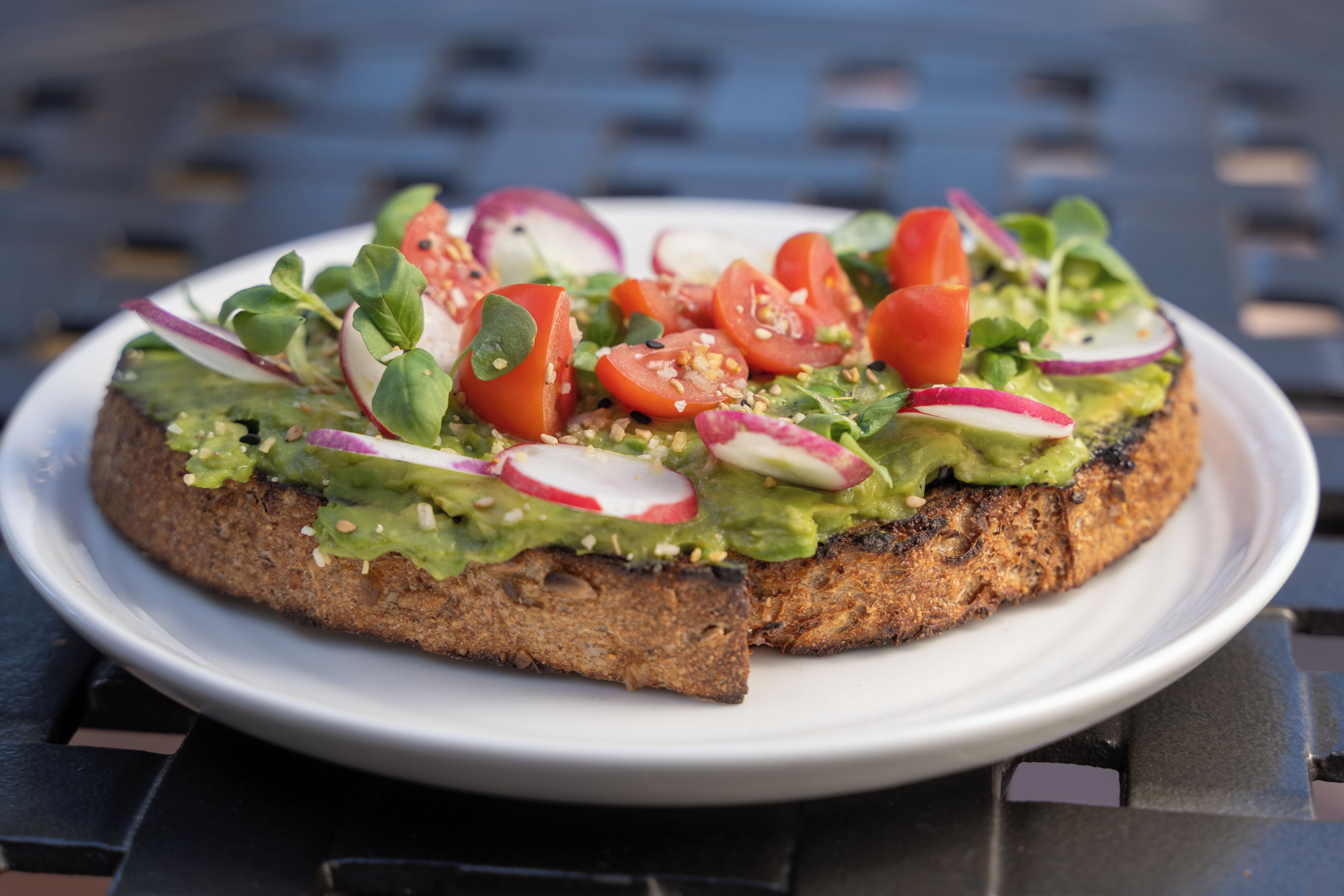 Un plato con un sándwich cubierto de aguacate, tomates, rábanos y verduras.