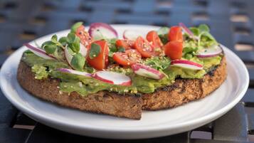 Un plato con un sándwich cubierto de aguacate, tomates, rábanos y verduras.
