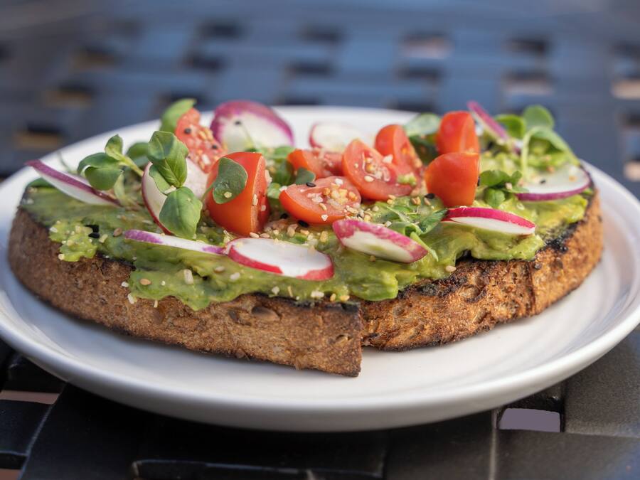 Un plato con un sándwich cubierto de aguacate, tomates, rábanos y verduras.