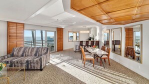 A spacious living area with a large window overlooking the ocean, a dining area with a table and chairs, and a sofa.