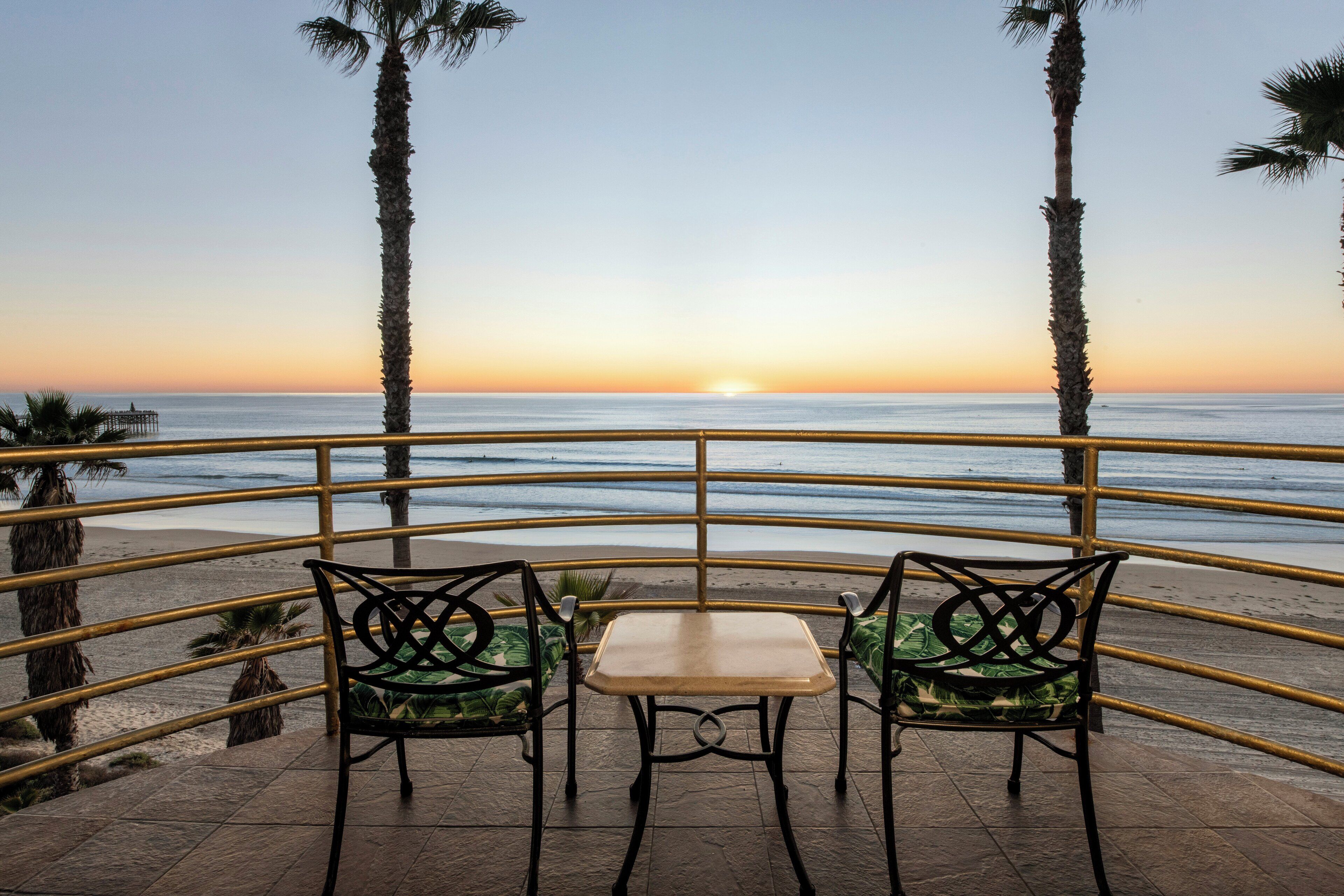 A terrace with two chairs and a table overlooking the ocean at sunset.