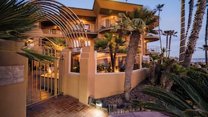A multi-story hotel with a curved entrance, palm trees, and a balcony with a railing.