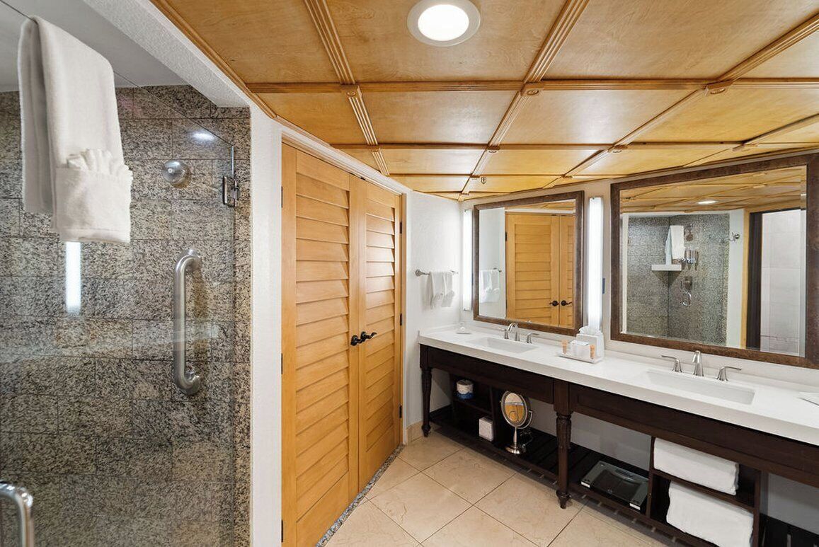 A bathroom with a wooden vanity, two sinks, a large mirror, and a shower area.