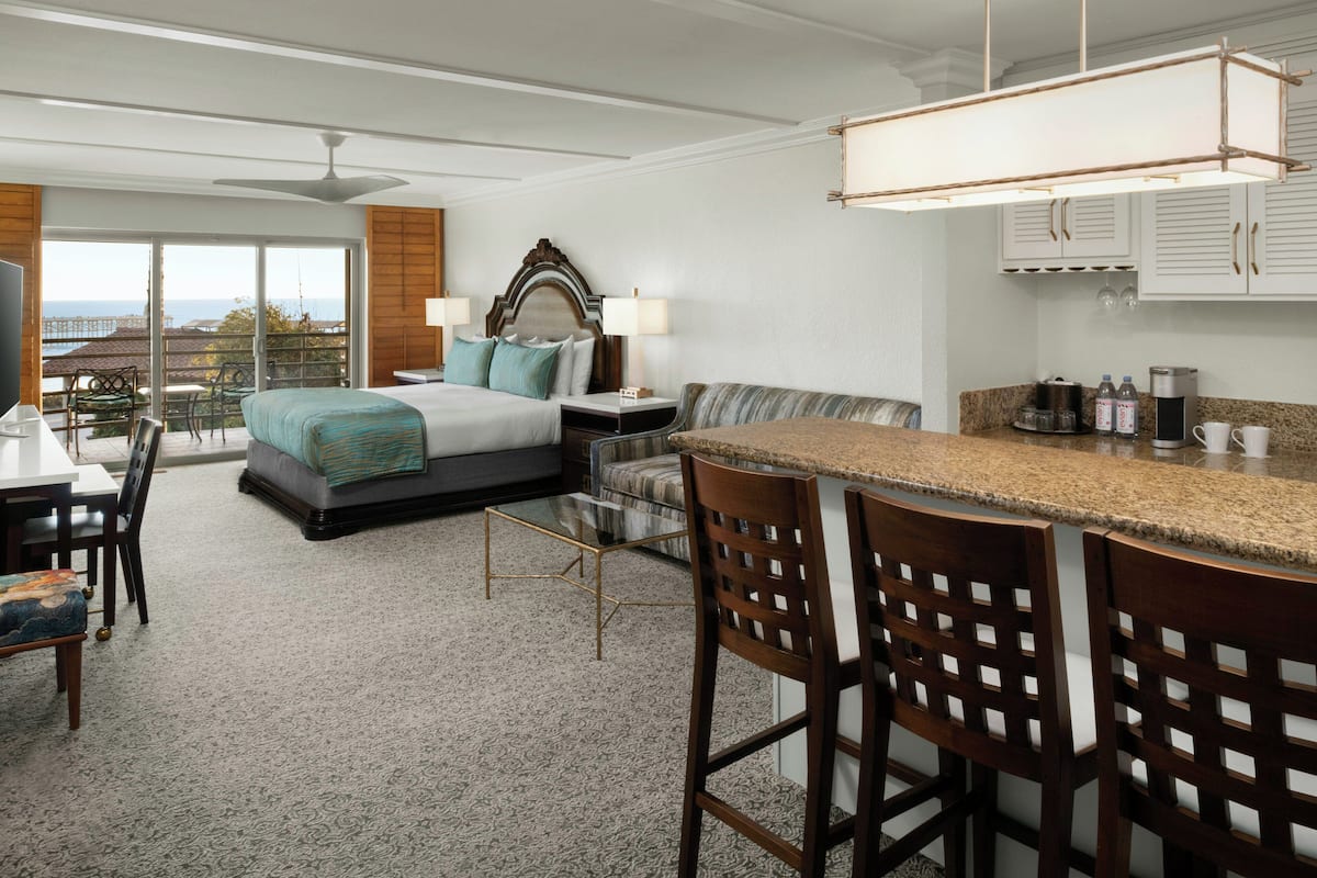 A hotel room with a bed, a desk, a bar area, and a view of the outdoors.