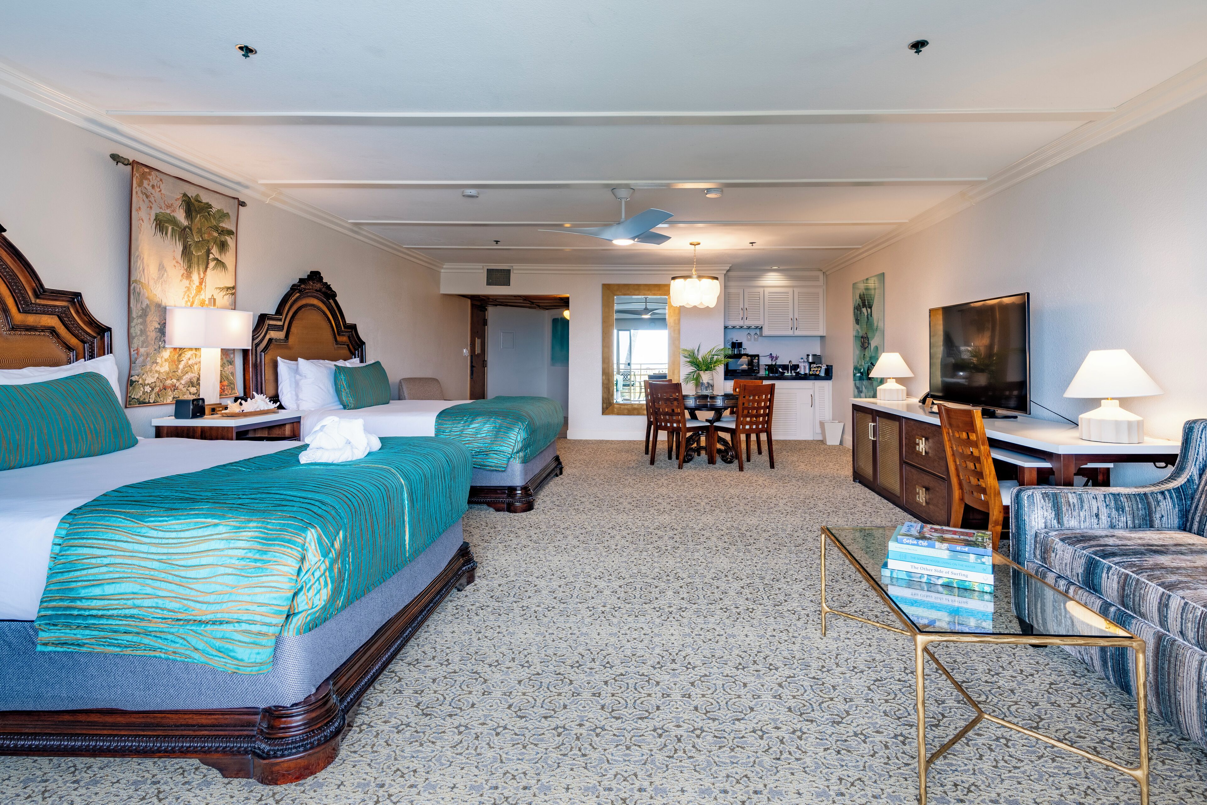 Habitación de hotel con una cama grande, dos camas más pequeñas, un comedor, una cocina y un televisor.