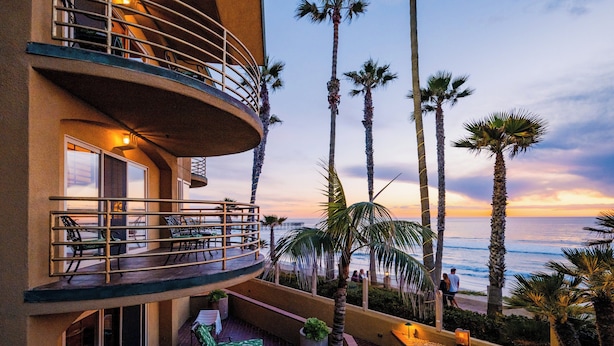 A hotel balcony with a curved railing, outdoor seating, and palm trees.
