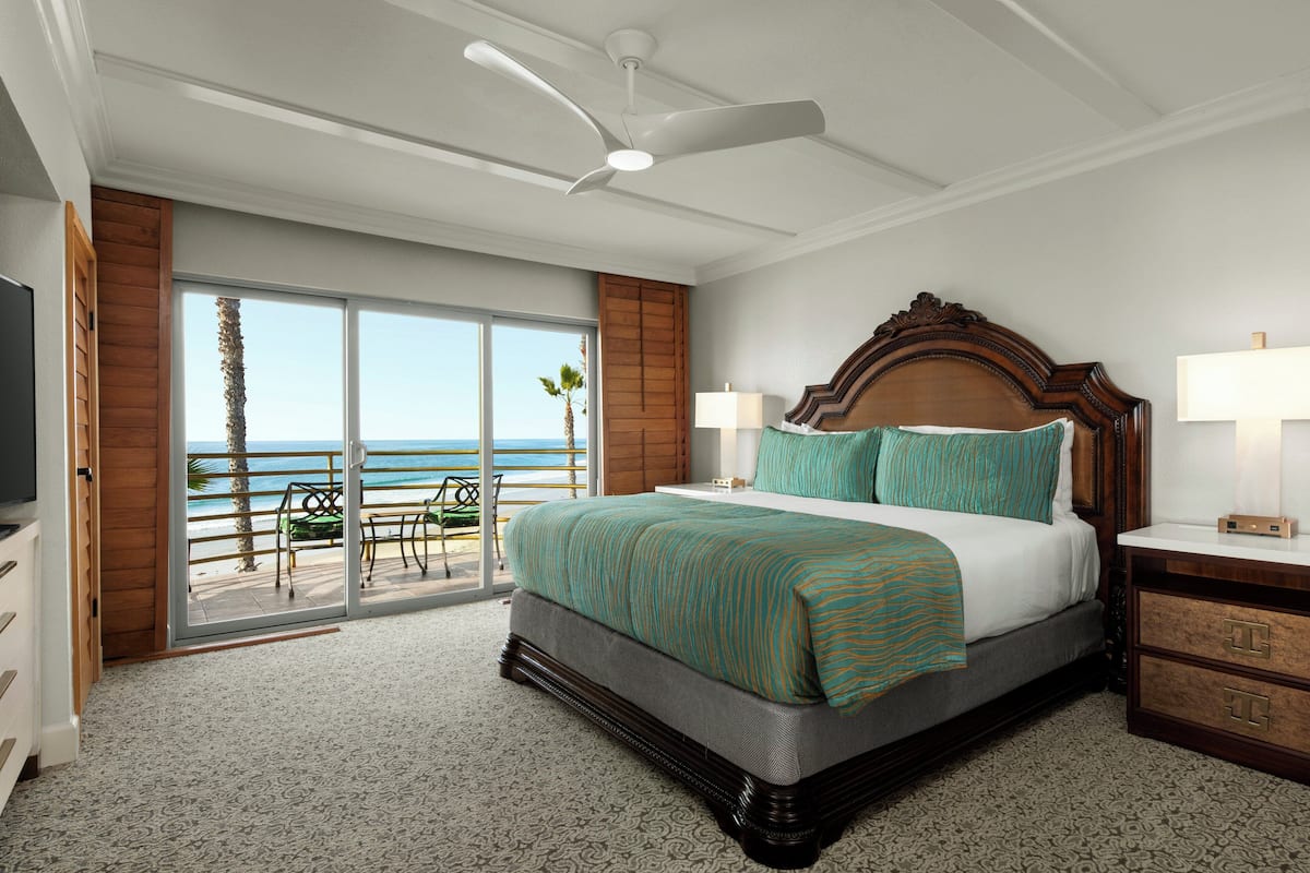 A spacious bedroom with a large bed, a ceiling fan, and a view of the ocean through a sliding glass door.