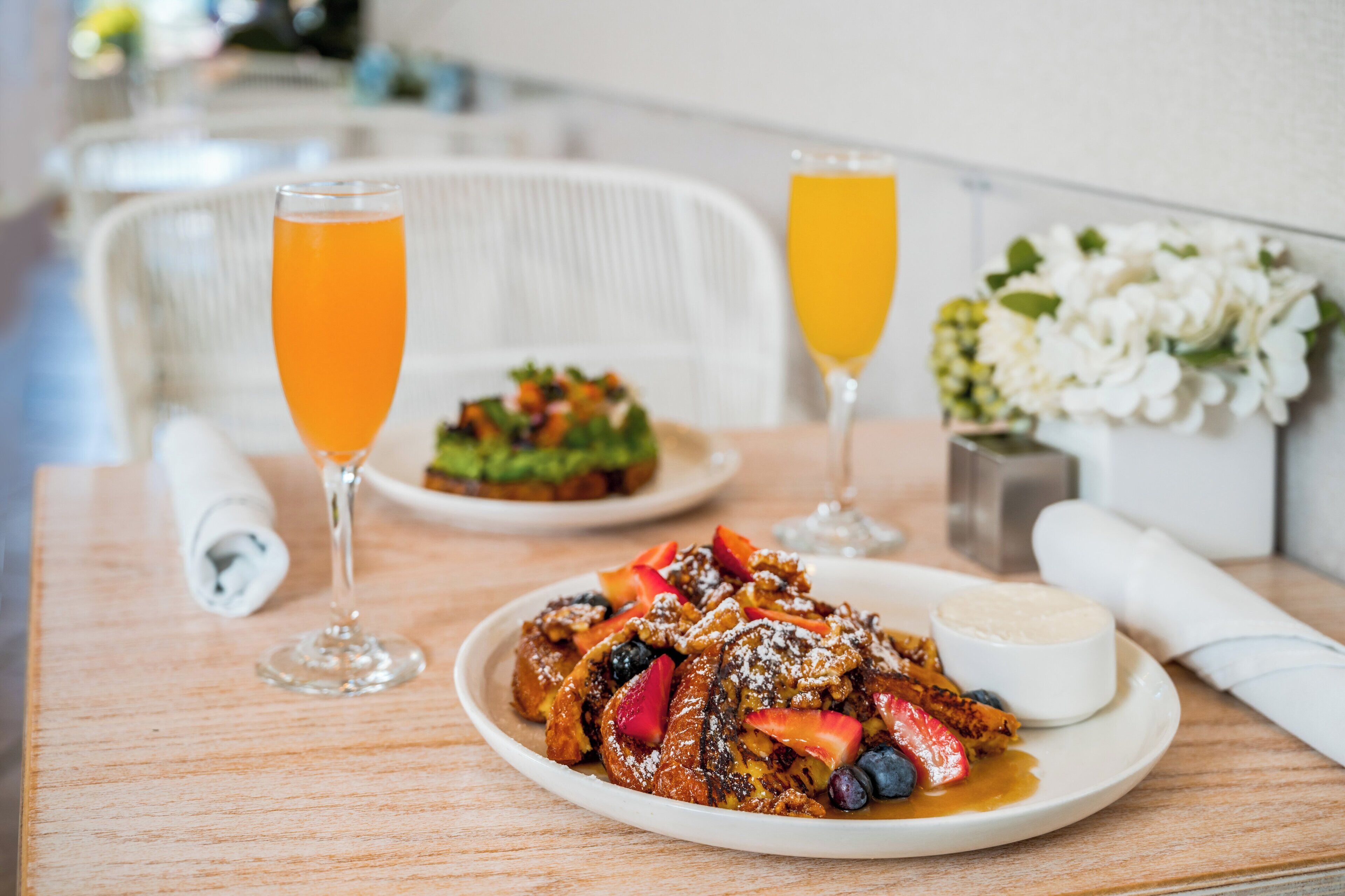Ein Frühstückstisch mit French Toast, einem Glas Orangensaft und einem weiteren Glas Orangensaft.