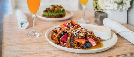 A breakfast setting with a plate of French toast, a glass of orange juice, and a glass of orange juice on a wooden table.