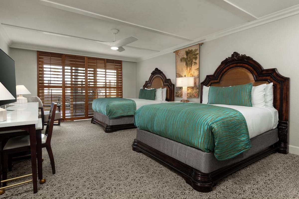 A hotel room with two beds, a desk, and a chair.