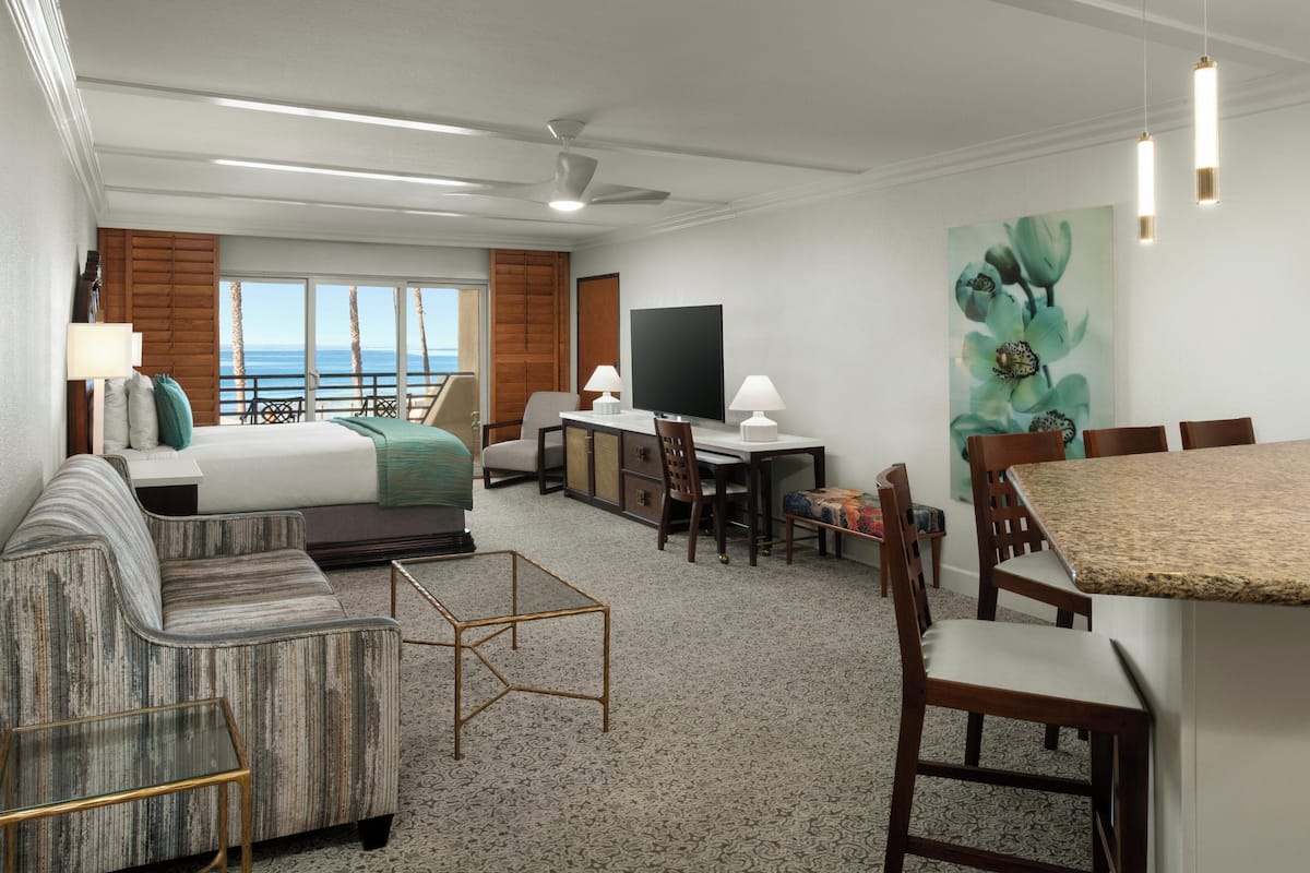 A hotel room with a bed, sofa, desk, chairs, and a dining table.