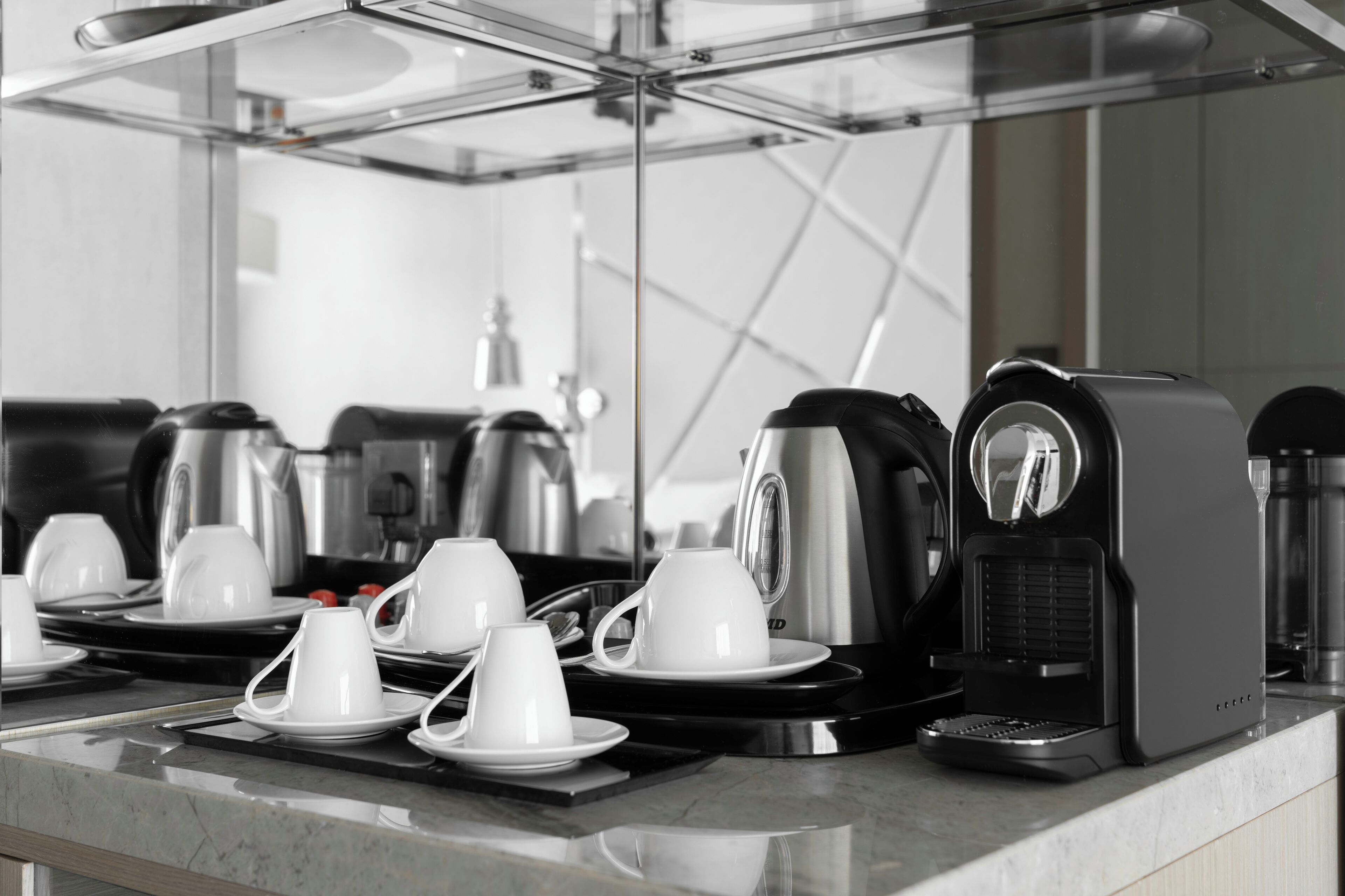 A coffee station with multiple coffee makers and white cups on a marble countertop.