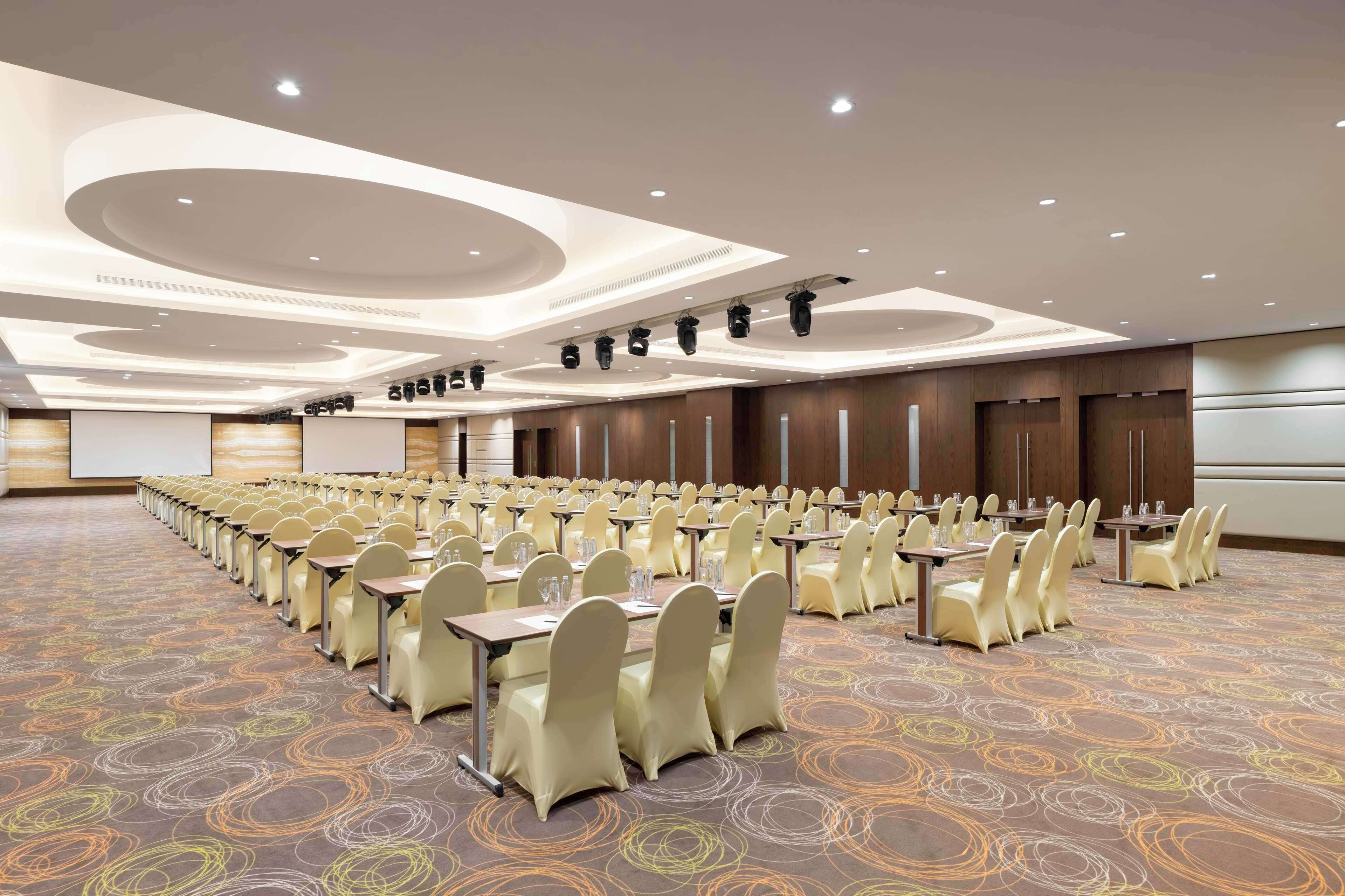 A conference room with rows of tables and chairs, a patterned carpet, and recessed lighting on the ceiling.