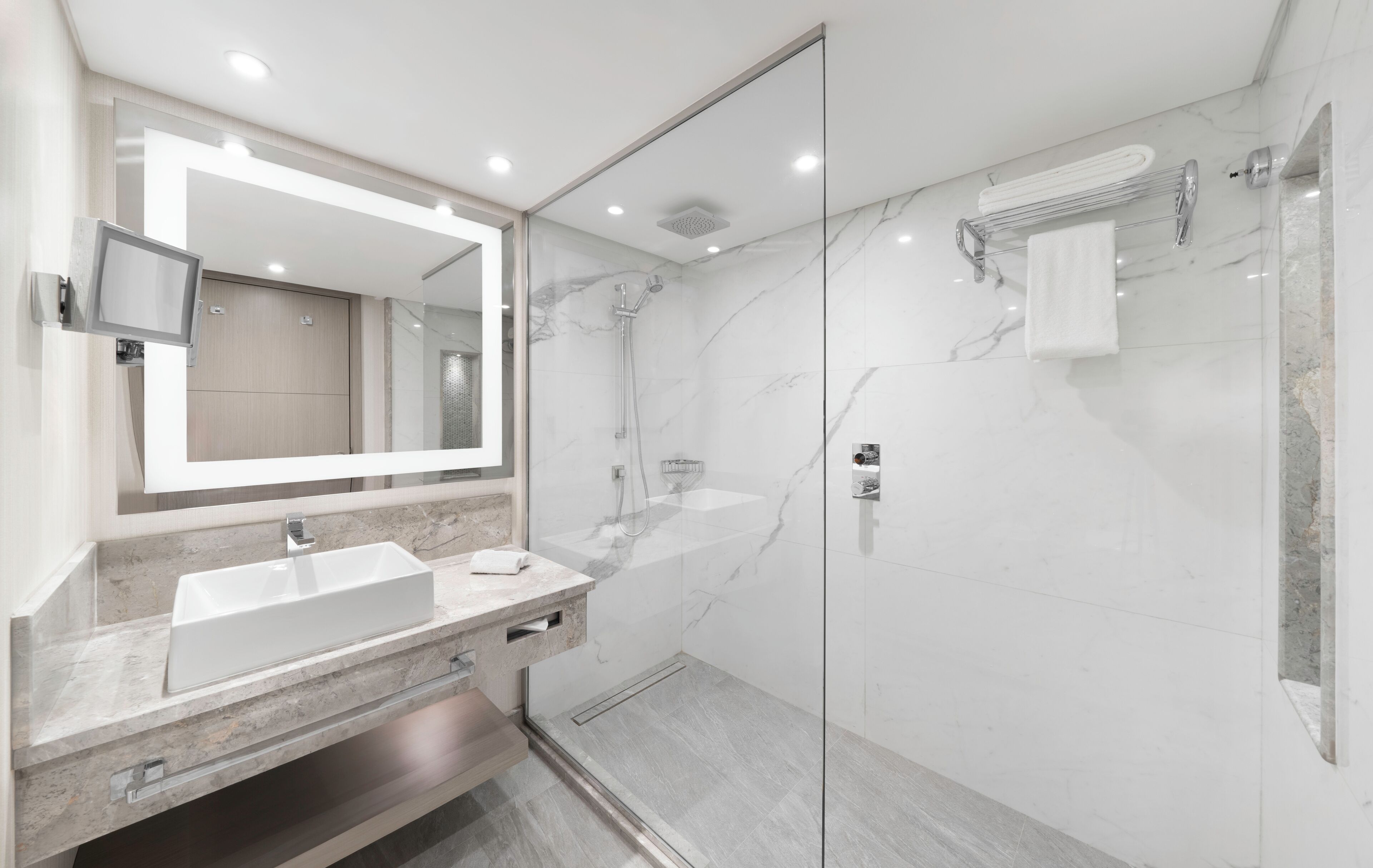 Un baño moderno con ducha envuelta en vidrio, un espejo grande y un mueble lavamanos doble.