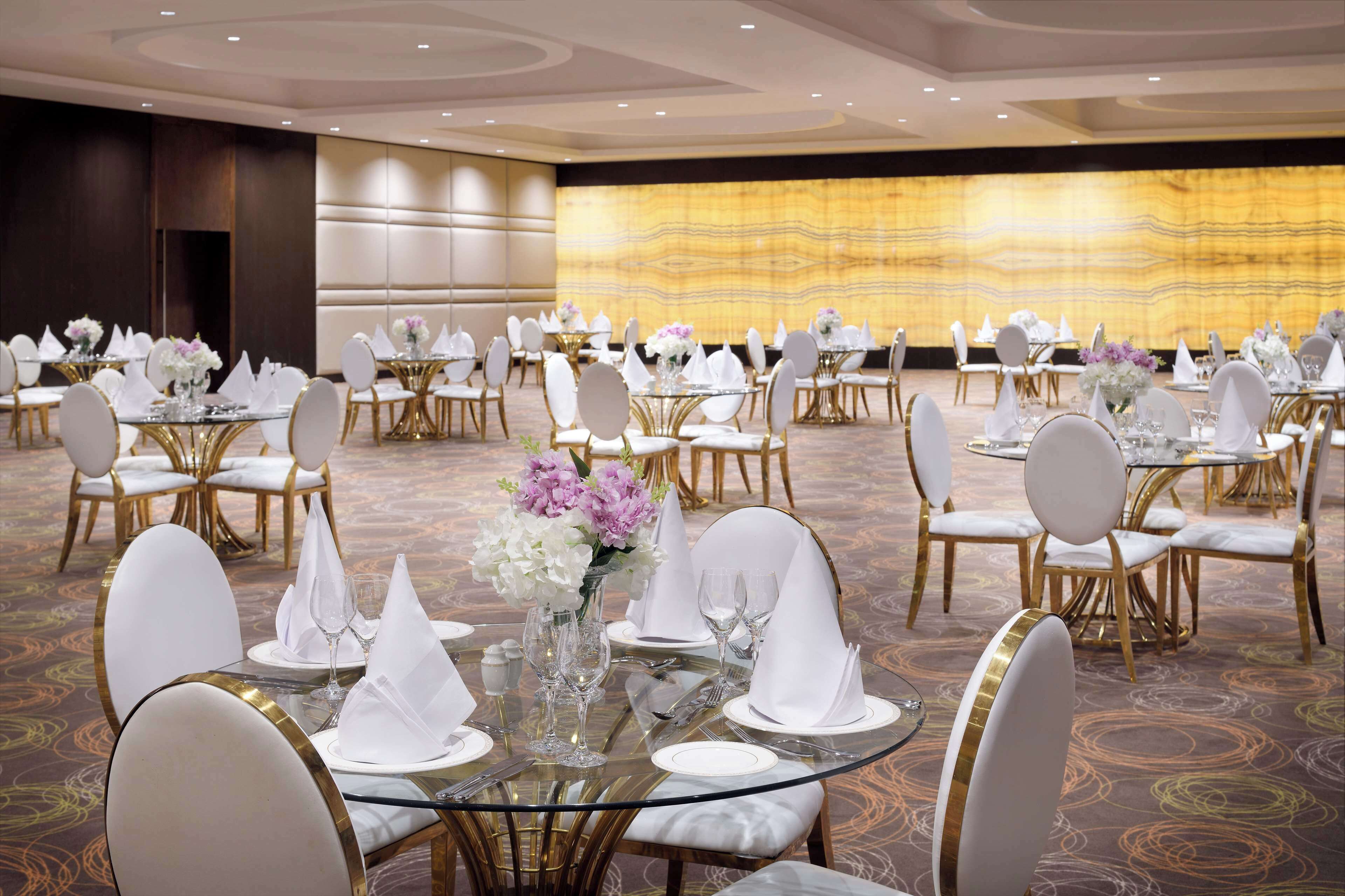 A banquet hall with round tables, white chairs, and gold accents.