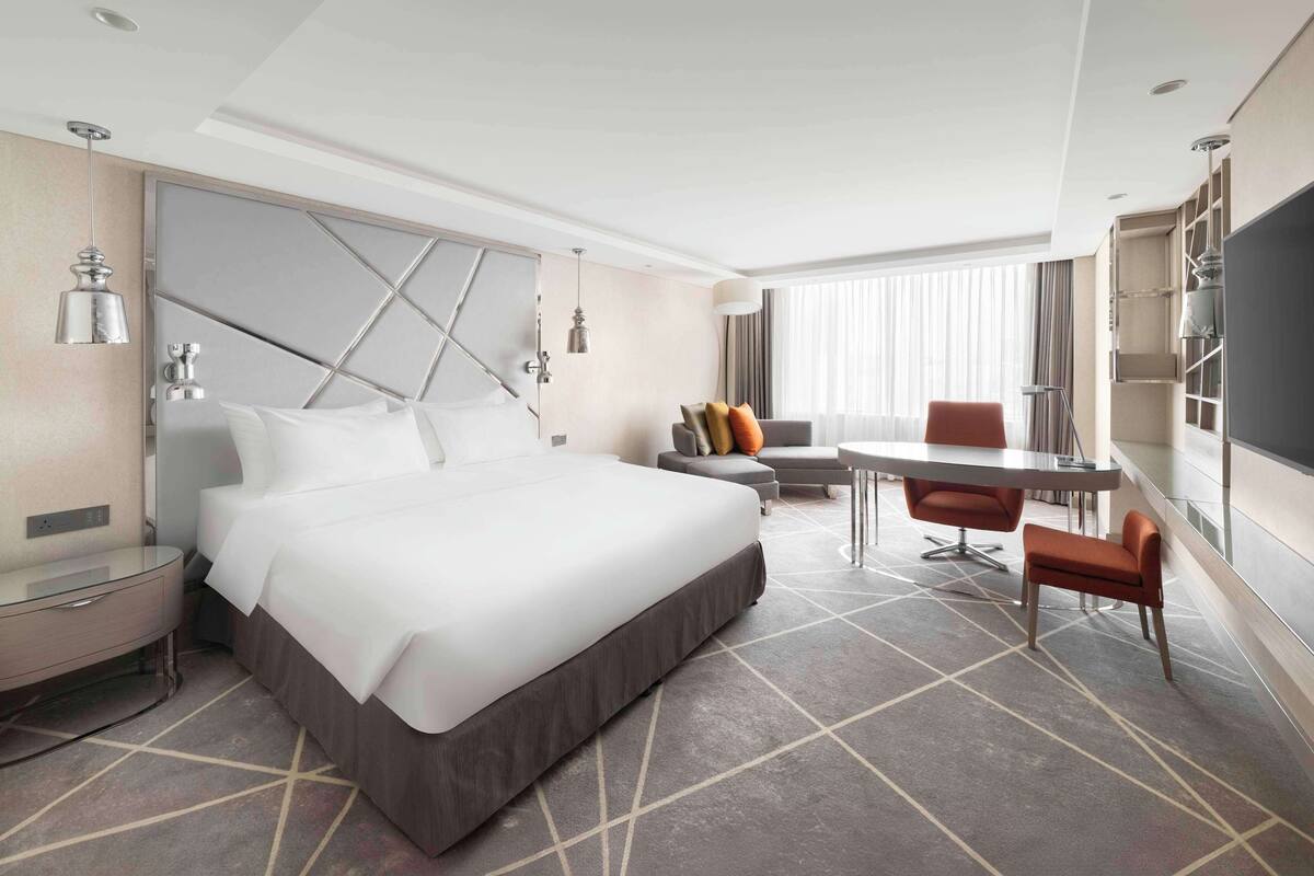 A modern hotel room with a large bed, a desk, and a chair.