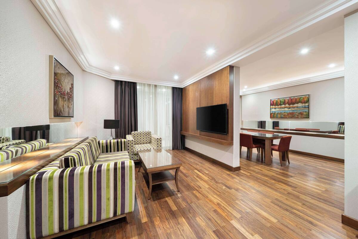 A modern living room with a sofa set, a coffee table, a TV mounted on the wall, and a dining area with a table and chairs.