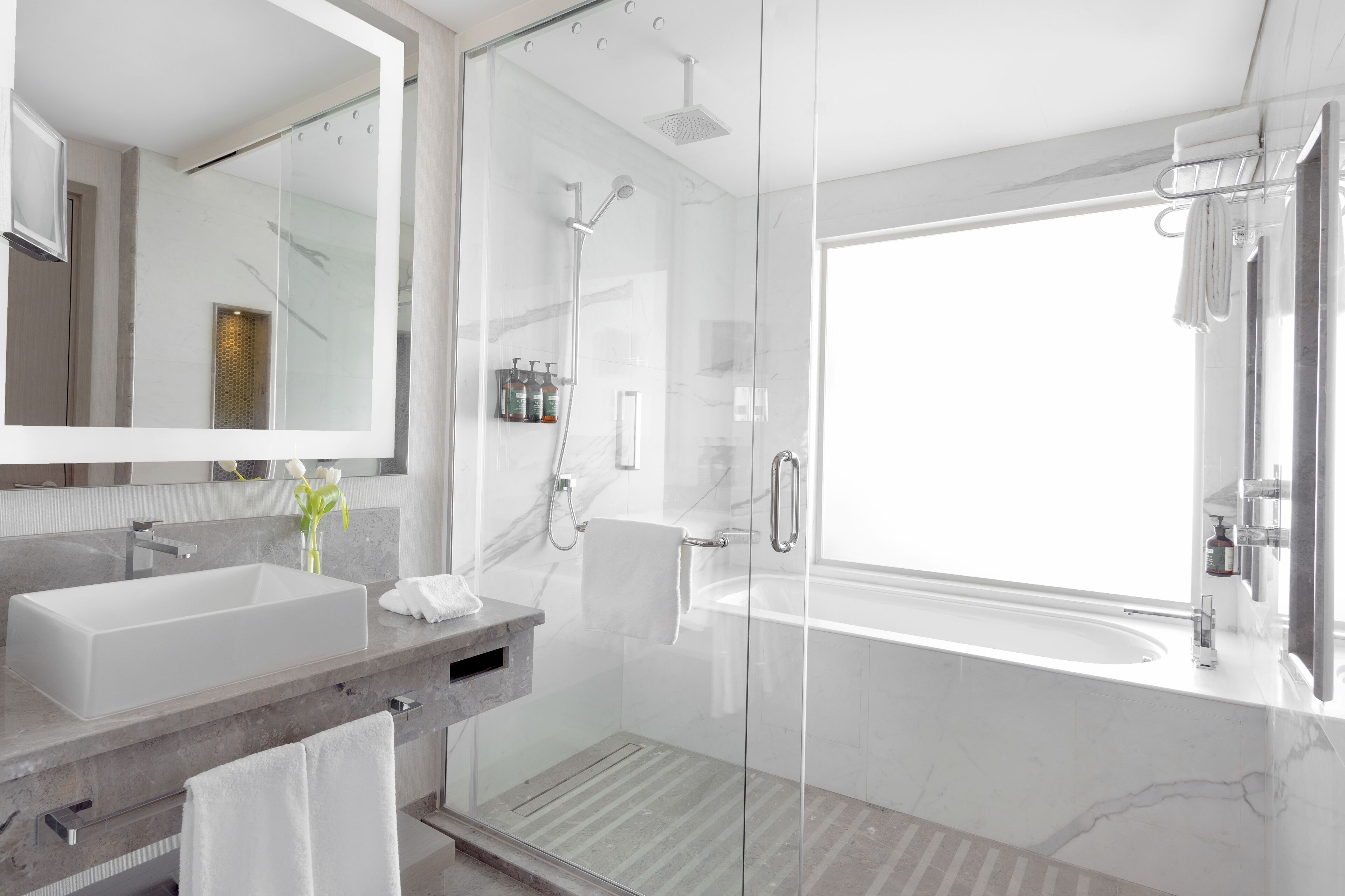 A modern bathroom with a glass-enclosed shower, a large bathtub, and a vanity with a sink and mirror.