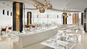 A modern restaurant with white furniture, a curved seating area, and decorative hanging lights.