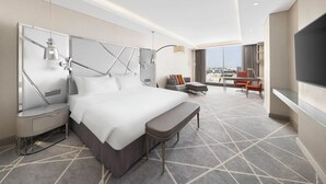 A modern hotel room with a large bed, a desk, a chair, and a TV.
