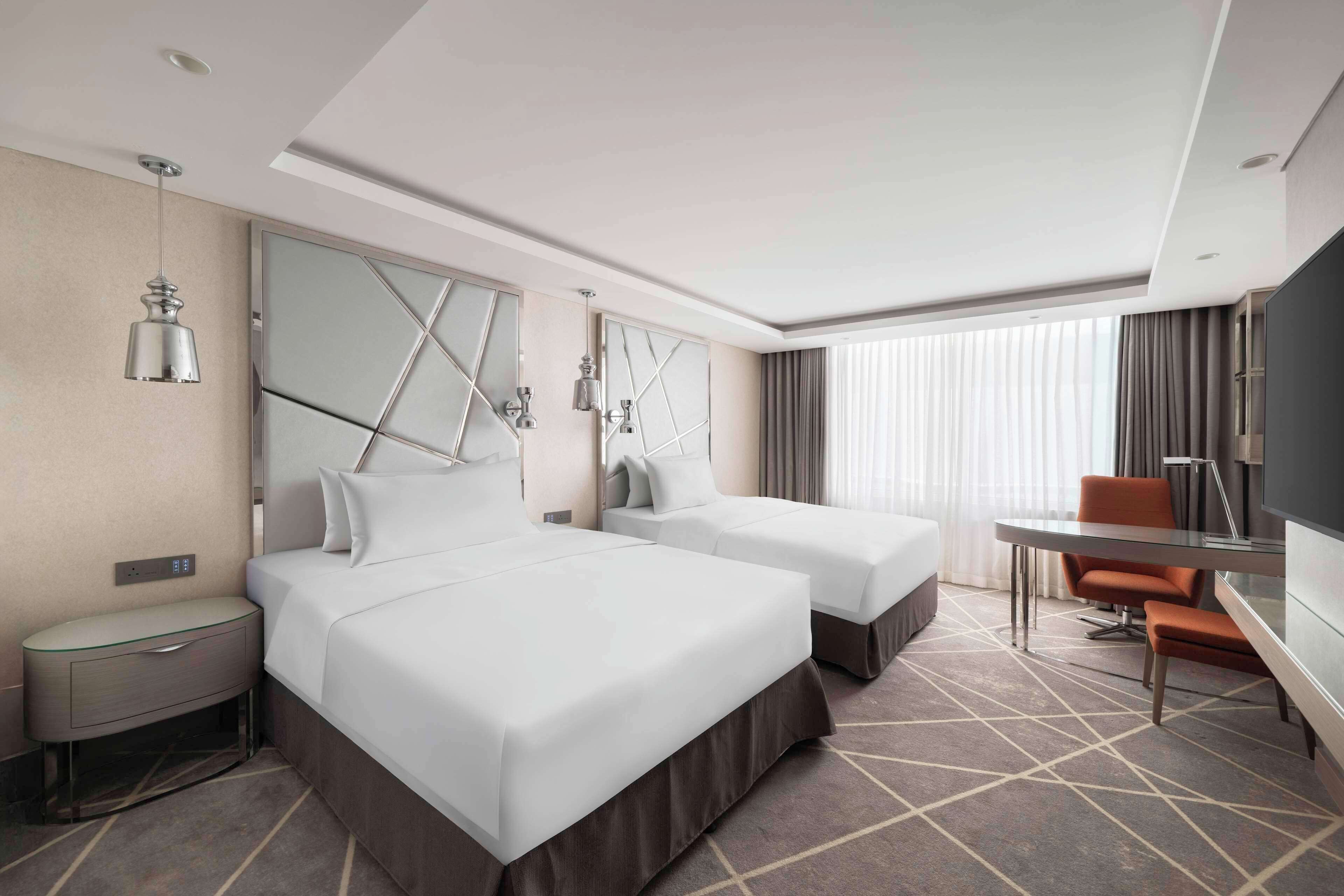A hotel room with two beds, a desk, and a TV.