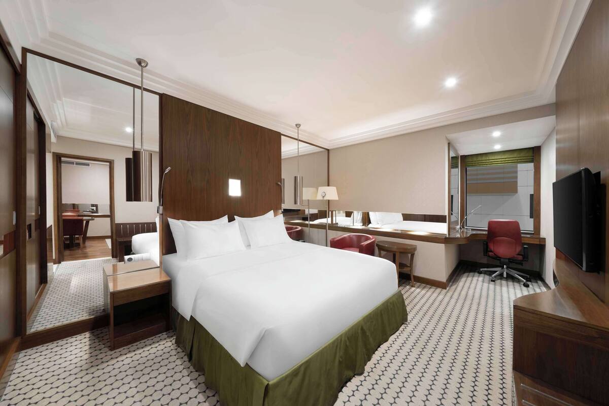 A hotel room with a large bed, a desk, a chair, a TV, and a bathroom visible through an open door.