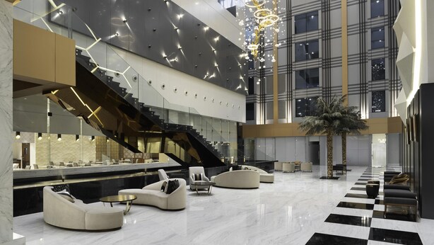 A spacious lobby with a checkered floor, modern seating, a staircase, and a decorative light fixture.