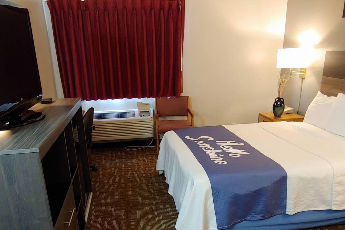 Une chambre d’hôtel avec un lit, un bureau, une télévision, une chaise, une lampe et un rideau rouge.