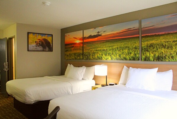 A hotel room with two beds, a nightstand with a lamp, and a large landscape painting above the beds.