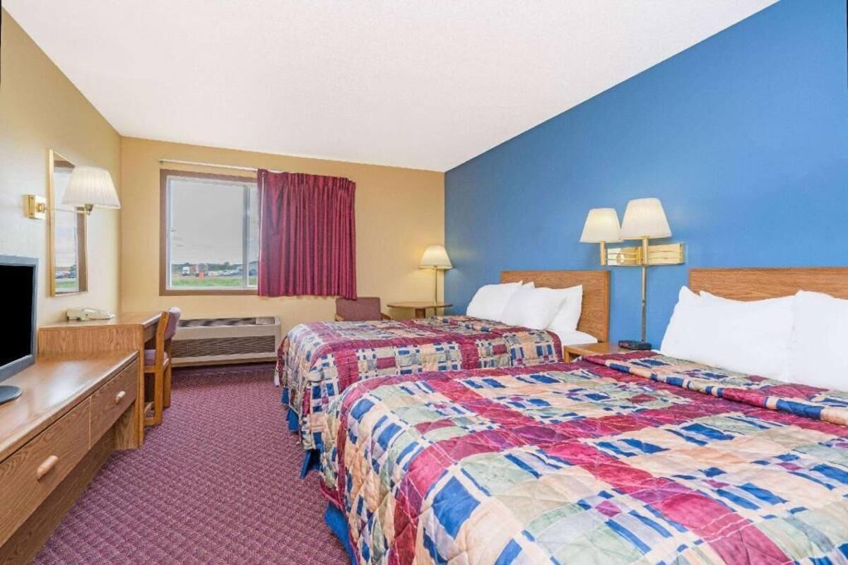 Une chambre d’hôtel avec deux lits, un bureau, une chaise, une télévision et une fenêtre avec des rideaux.