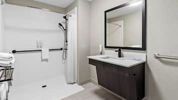 A modern bathroom with a walk-in shower, a large mirror, and a vanity with a sink.