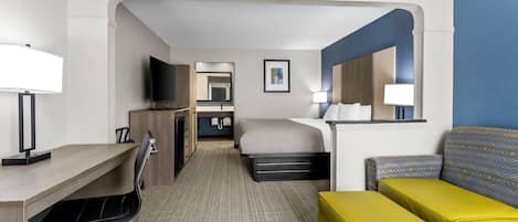A hotel room with a desk, a bed, a sofa, a TV, and a mirror.