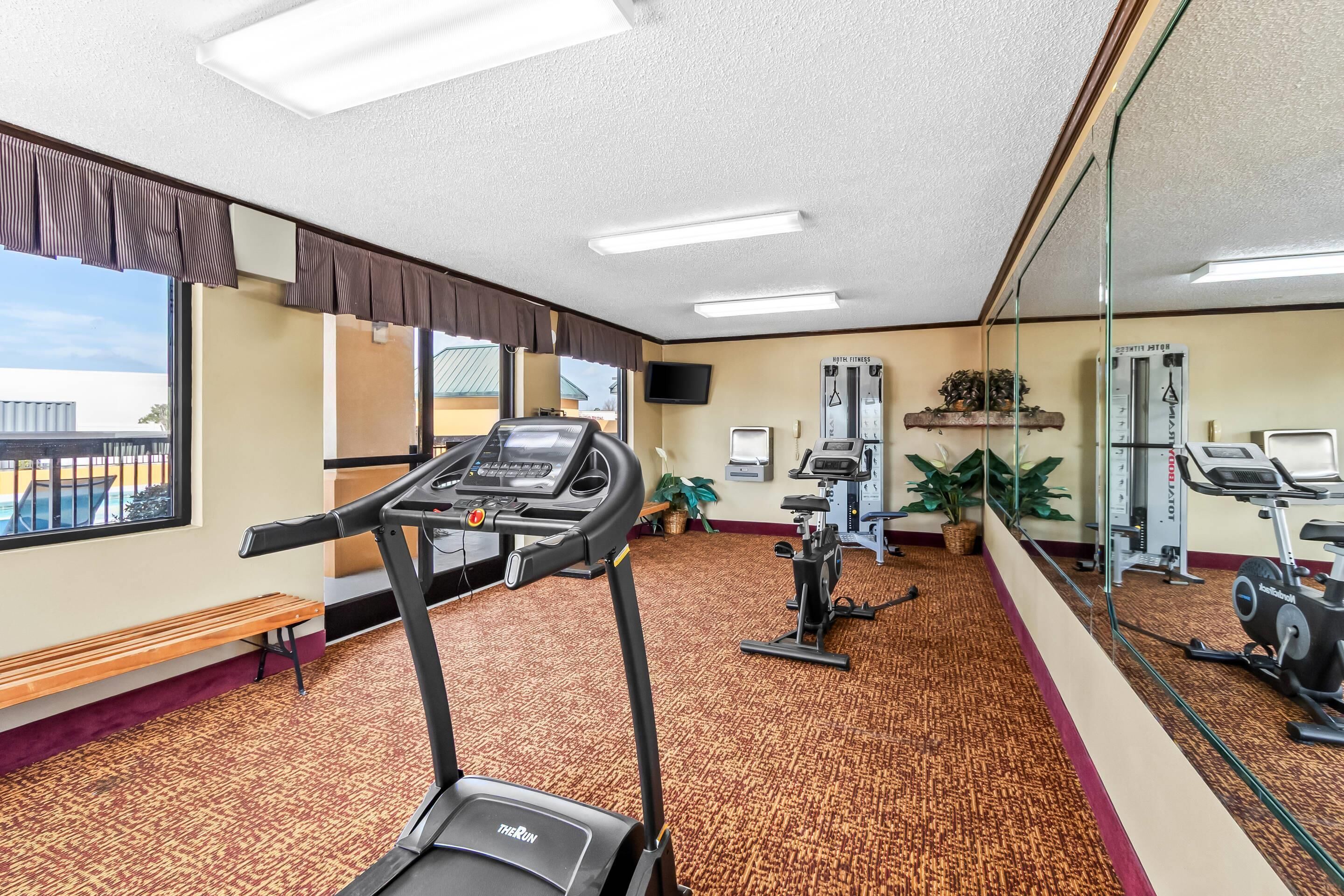 Academia com esteiras, máquinas de exercício, um banco e um espelho grande.