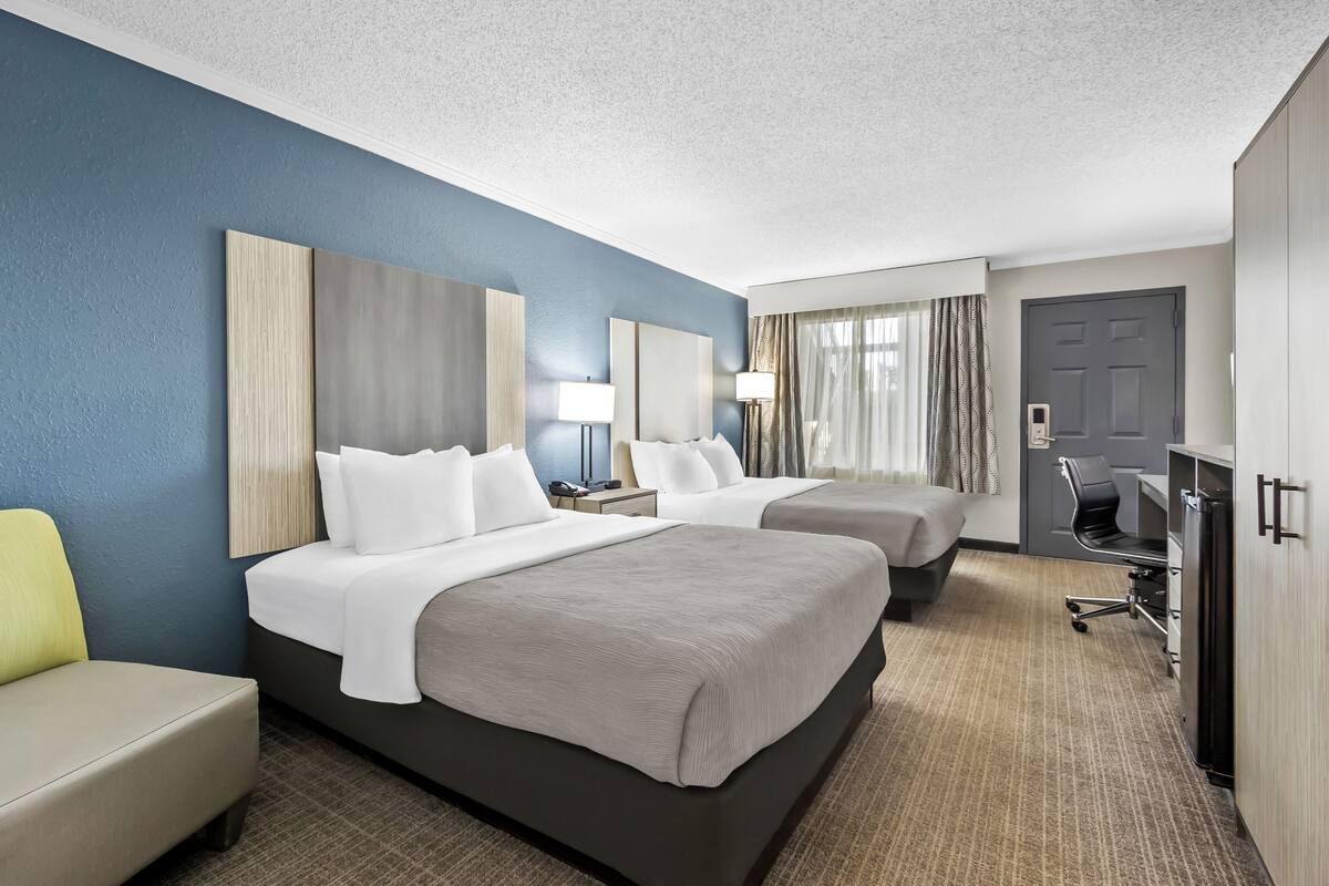 A hotel room with two beds, a desk, a chair, and a wardrobe.
